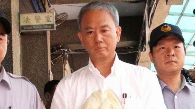 Ngụy Ưng Sung, một torng bốn chủ tịch của tập đoàn thực phẩm quốc tế Đỉnh Tân đang bị cảnh sát áp giải - Ảnh:AFP