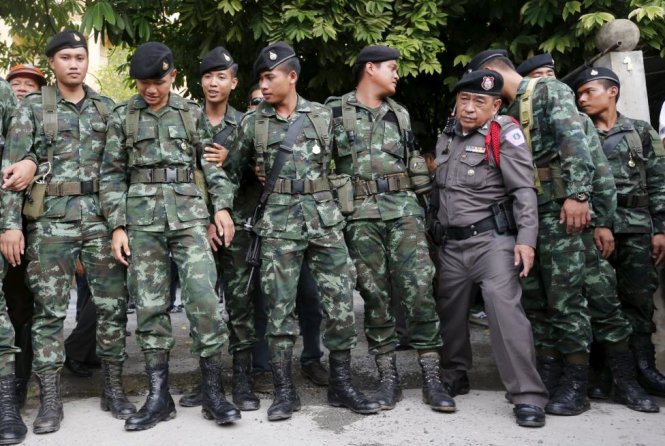 Một quan chức cảnh sát Hoàng gia Thái Lan (trang phục nâu) đi qua các binh sĩ quân đội Thái Lan tại địa điểm bắt giữ nghi phạm gần đây - Ảnh: Reuters