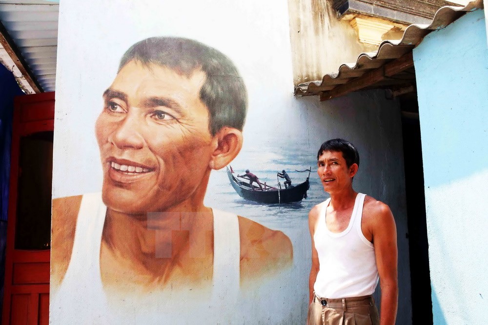 Ông Võ Ngọc Liêm bên chân dung của mình trên bức tường tại làng chài Trung Thanh. (Ảnh: Trần Lê Lâm/TTXVN)