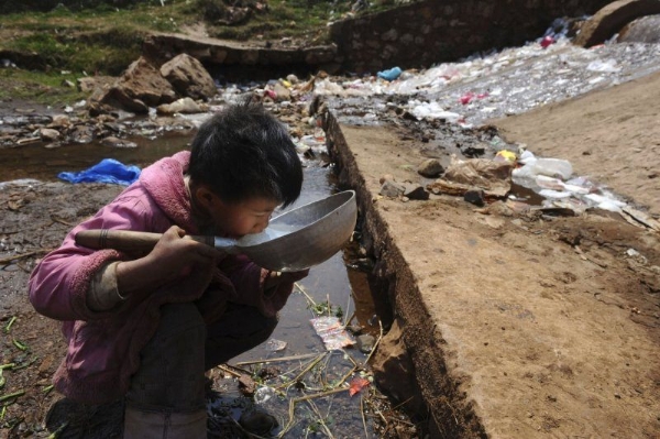 Cậu bé uống nước từ một dòng nước chứa đầy rác thải.