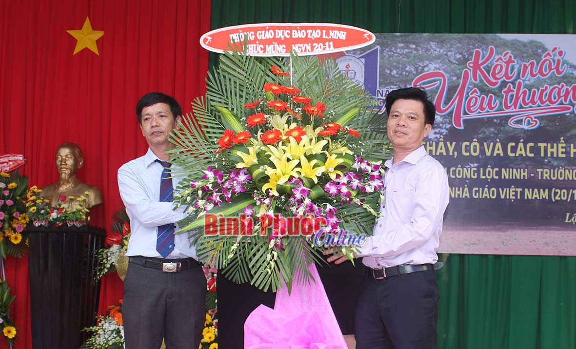 Thầy Hà Văn Sĩ (bên trái) nhận hoa chúc mừng của Phòng GD-ĐT huyện Lộc Ninh dịp 20-11